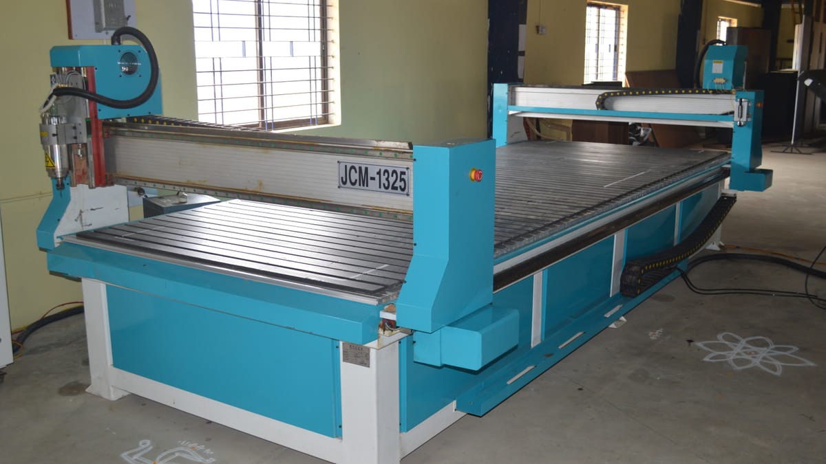 A blue JCM-1325 CNC router with gantry and spindle head standing in a workshop bay.