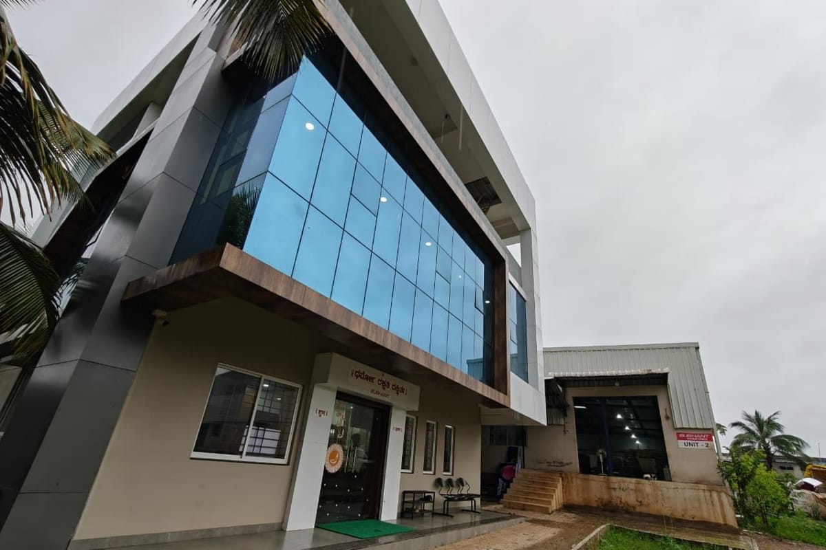 Three-storey Sushant Industries office with blue glass curtain wall, entrance canopy and the Unit 2 shed beside it