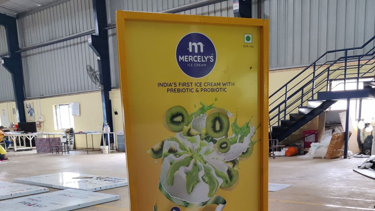 Mercely's kiwi ice cream standee in a yellow steel frame on the floor of a steel-framed fabrication shed.