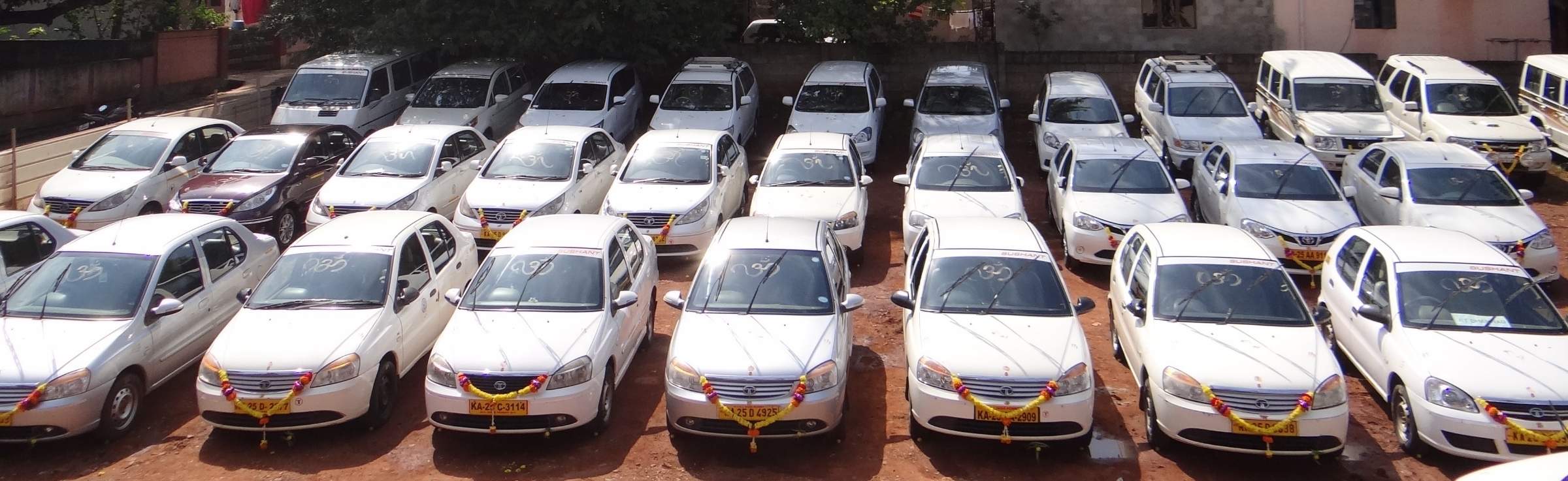 Rows of garlanded Sushant Travels & Logistics sedans in the Dharwad yard