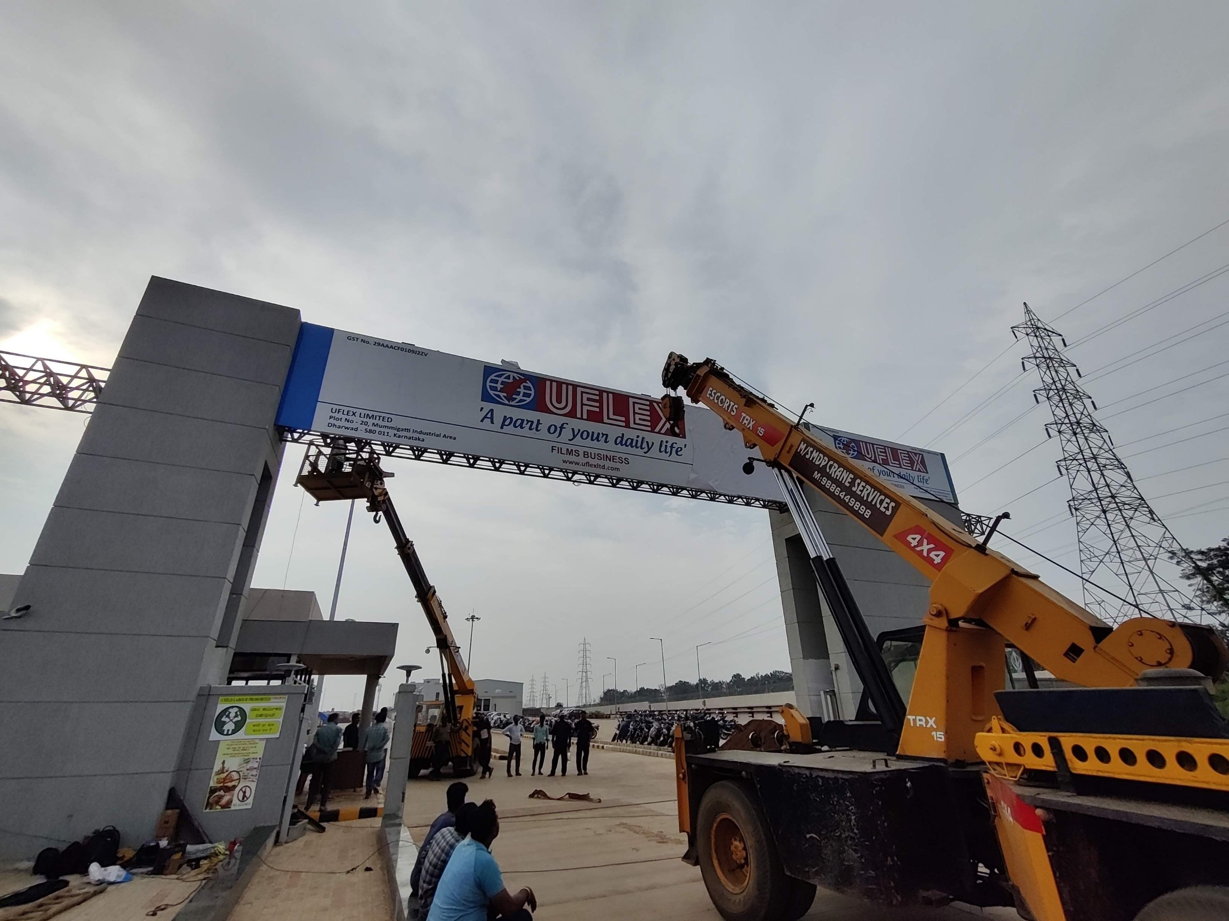 A crane lifting a gantry sign into place at a Dharwad industrial entrance